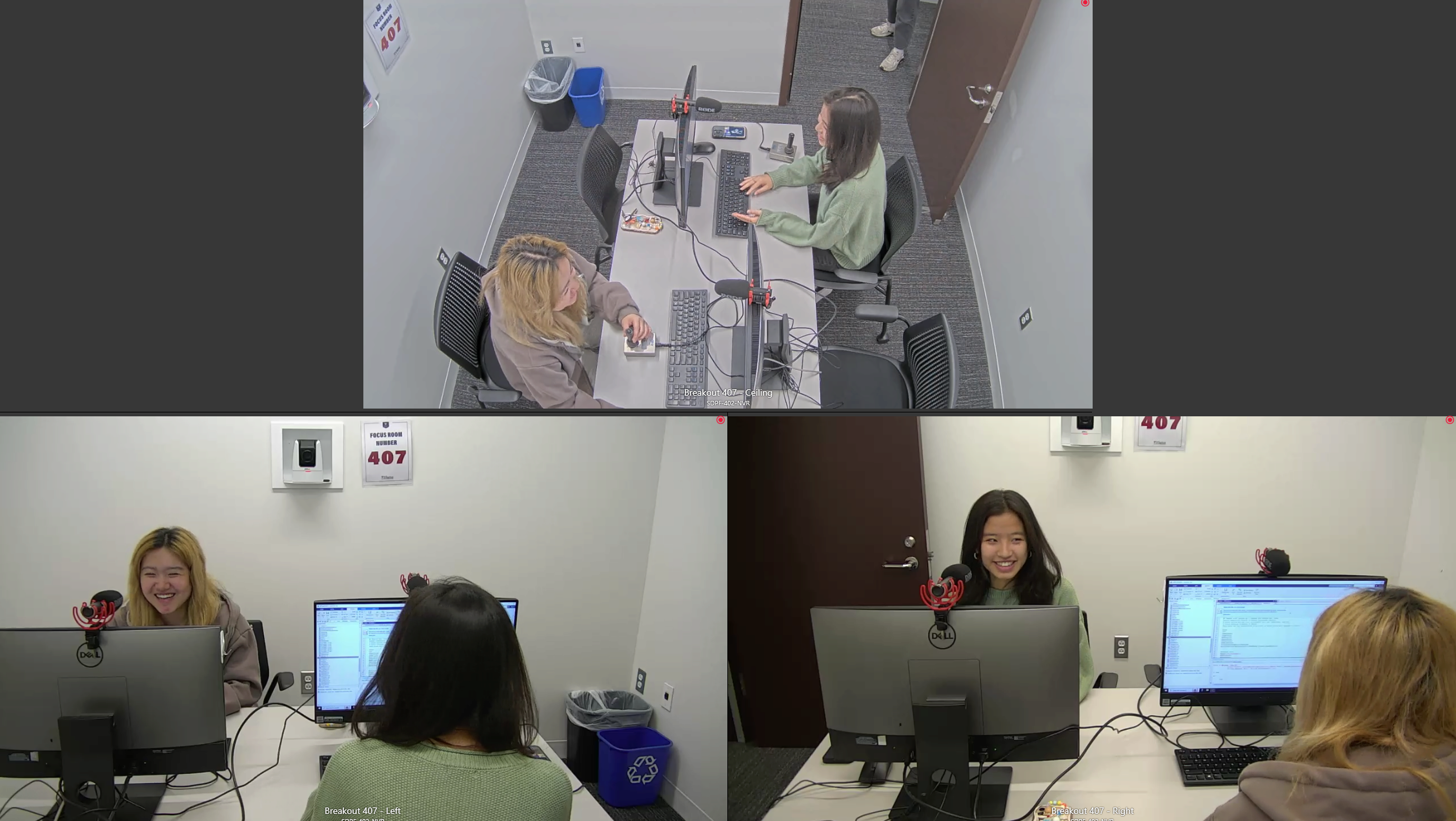 A split-screen view of two people working at a desk with computers and microphones in a small office or study room. They appear to be engaged in conversation or discussing work.