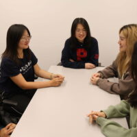 A small group of people sitting around a table, engaged in conversation. They appear relaxed and are smiling, suggesting a friendly discussion or meeting.