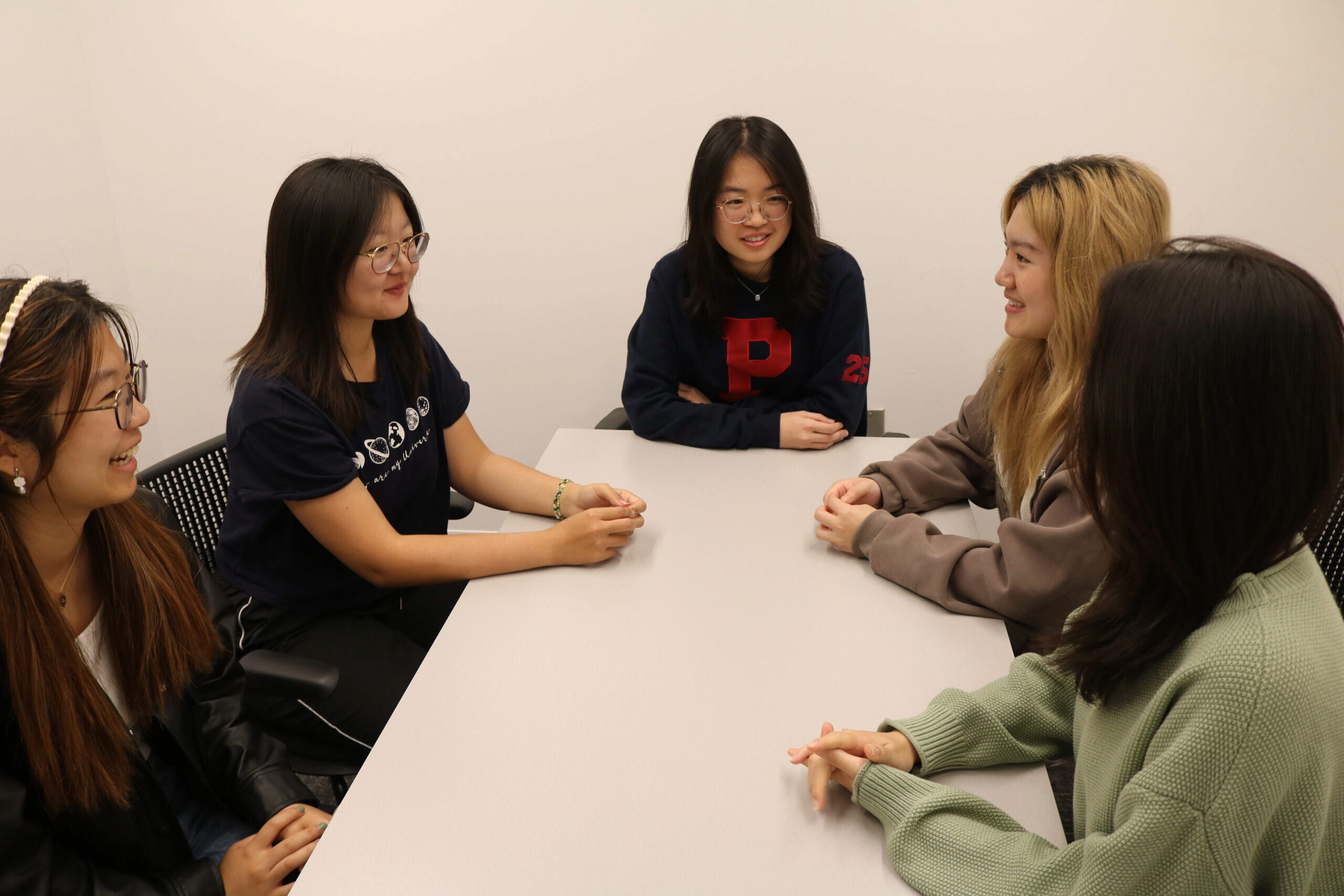 A small group of people sitting around a table, engaged in conversation. They appear relaxed and are smiling, suggesting a friendly discussion or meeting.