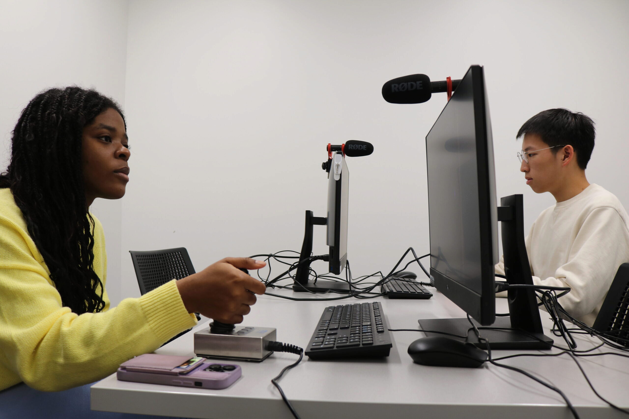 Two people in a lab setting using computers with microphones attached, engaged in an apparent experiment or study involving technology and communication.