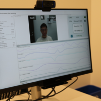 A computer monitor displaying biometric data from sensors related to facial expression analysis and emotional engagement, with a webcam view of a person and graphs charting various measured metrics.