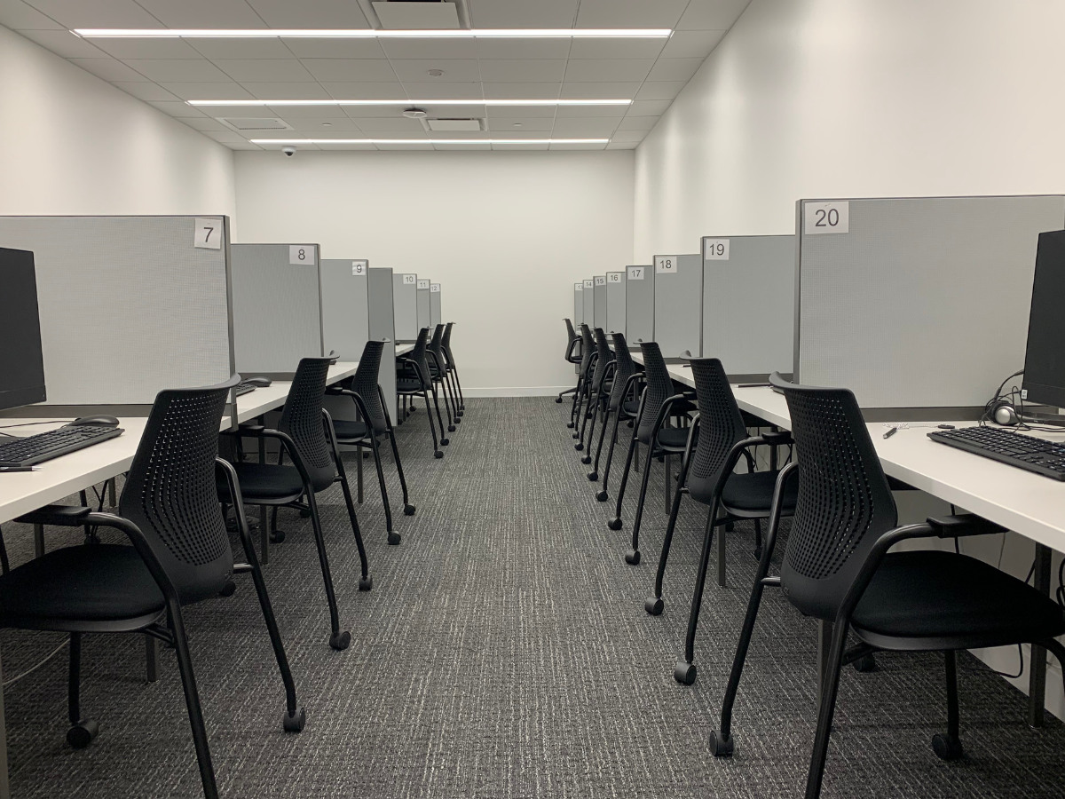 A room with workstations featuring computers and numbered partitions, arranged in two rows. Black chairs are placed at each desk, creating a structured and organized environment.