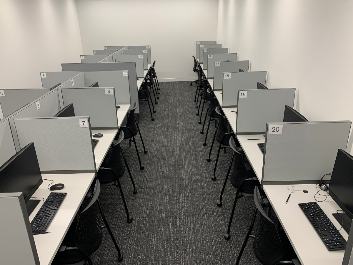 A room with rows of computer workstations separated by grey dividers. Each station has a monitor, keyboard, and mouse. The area appears organized and suitable for office work or study.