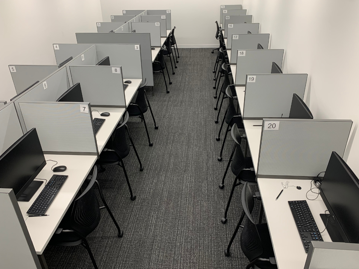 A room with rows of partitioned cubicles, each equipped with a computer, keyboard, and mouse. The cubicles have numbers for identification, likely representing a call center or computer lab setup.