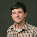 Headshot of person wearing a plaid shirt against a plain background.